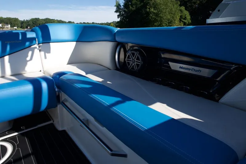 Slide: The Image of 2017 MasterCraft X26 boat interior with blue and white seating, speaker, and lush greenery background. - 18