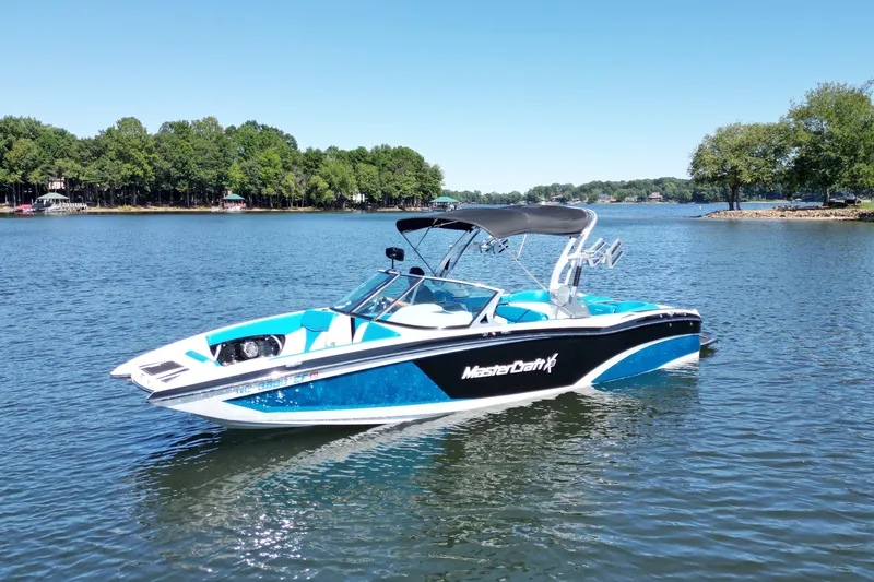 Slide: The Image of 2017 MasterCraft X26 boat on a serene lake with lush green shoreline. - 3