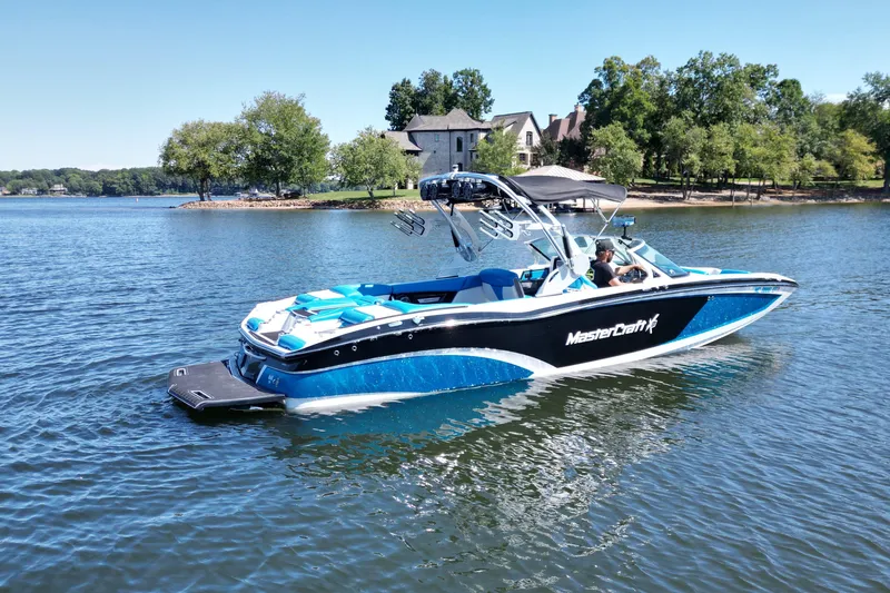Slide: The Image of 2017 MasterCraft X26 boat on a serene lake with lush greenery. - 5