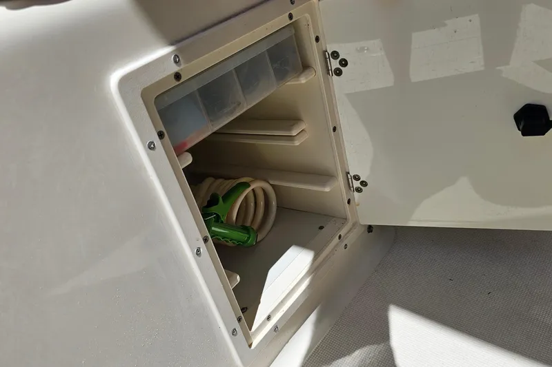 Slide: The Image of Open storage compartment on a 2004 Pursuit 3070 Express boat, containing coiled hose and organizer. - 25