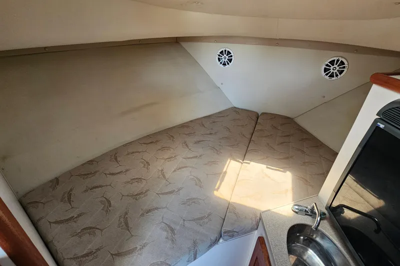 Slide: The Image of 2004 Pursuit 3070 Express cabin interior with bed, sink, and speakers. - 28