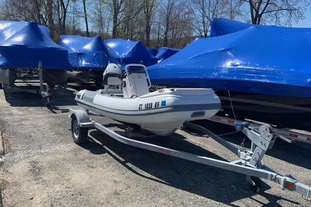 Slide: The Image of 2023 Highfield Sport 330 inflatable boat on trailer, surrounded by blue-covered boats. - 14