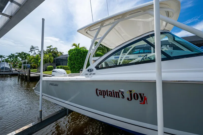 Slide: The Image of 2022 Pursuit DC 246 Dual Console boat docked, named "Captain's Joy," in a scenic marina. - 2