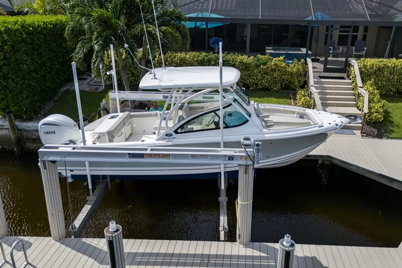 Slide: The Image of 2022 Pursuit DC 246 Dual Console boat docked on a lift near a waterfront home. - 36