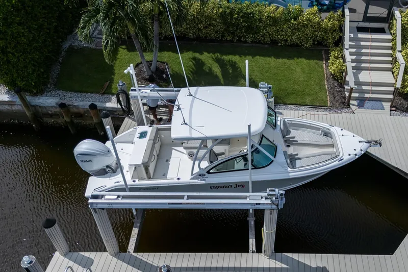 Slide: The Image of 2022 Pursuit DC 246 Dual Console boat on lift, docked near lush greenery. - 9