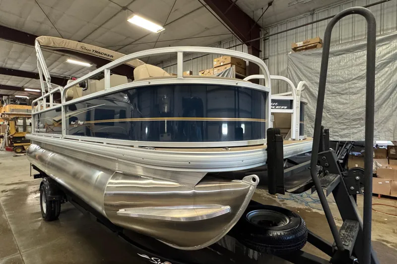 Slide: The Image of 2025 Sun Tracker Bass Buggy 18 DLX pontoon boat in a warehouse setting. - 2