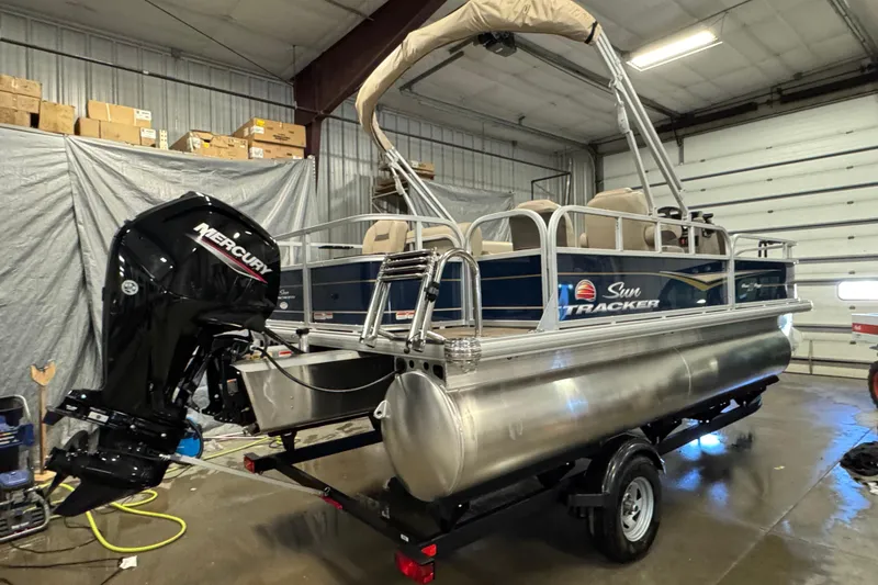 Slide: The Image of 2025 Sun Tracker Bass Buggy 18 DLX pontoon boat with Mercury outboard motor in a garage. - 3