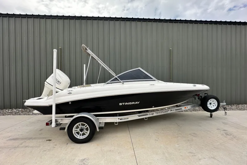 Slide: The Image of 2019 Stingray 191 DC boat on trailer, parked outdoors against a metal building. - 4