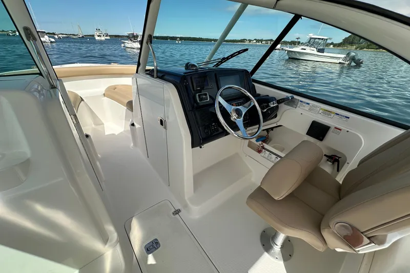 Slide: The Image of 2015 Pursuit DC 265 Dual Console boat interior with steering wheel, beige seating, and water view. - 13
