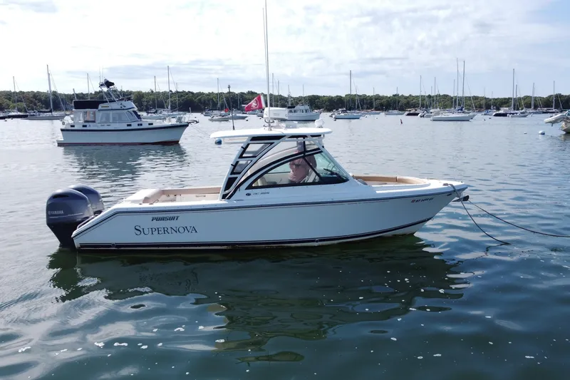 Slide: The Image of 2015 Pursuit DC 265 Dual Console boat on calm water, surrounded by other vessels. - 2