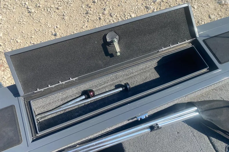 Slide: The Image of 2017 Tracker Targa V-18 WT boat storage compartment with rod holder, open on gravel surface. - 7