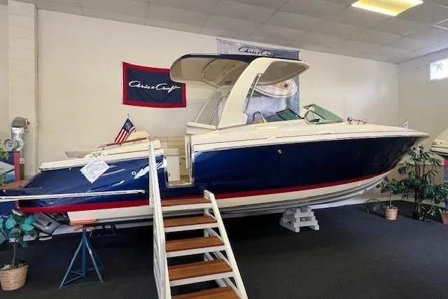 The Image of 2025 Chris-Craft Launch 28 GT boat displayed indoors with American flag and stairs. - 0
