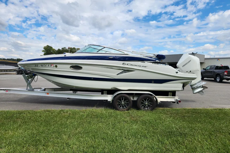 Slide: The Image of 2024 Crownline Eclipse E240 XS boat on trailer, parked outdoors under a partly cloudy sky. - 6