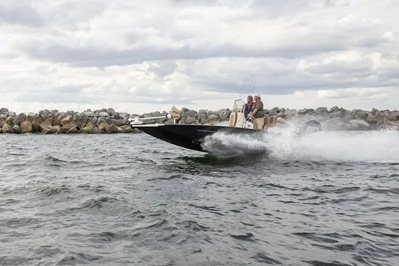 Slide: The Image of 2026 Xpress H22B Bay boat speeding on water near rocky shoreline. - 31