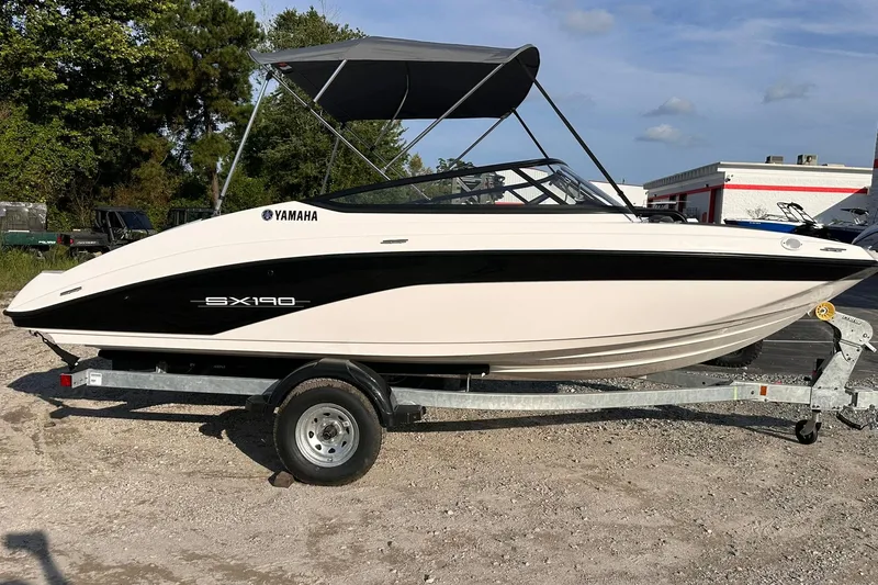 The Image of 2025 Yamaha Boats SX190 on trailer, featuring sleek design and canopy, parked outdoors. - 0