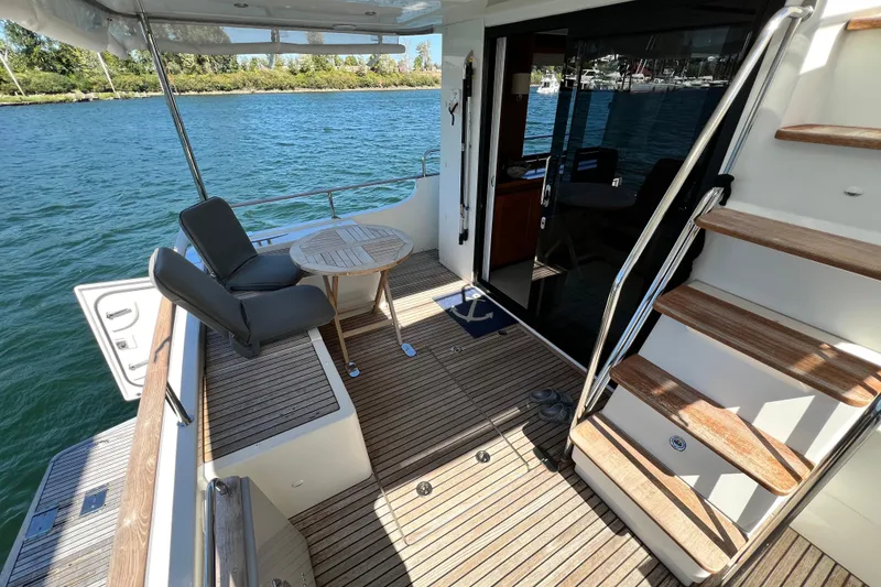 Slide: The Image of 2014 Beneteau Swift Trawler 50 deck with seating, table, and stairs by the water. - 10