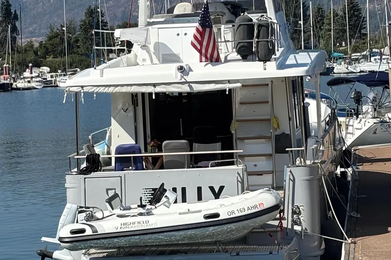 Slide: The Image of 2014 Beneteau Swift Trawler 50 docked with dinghy, American flag, and scenic marina backdrop. - 52