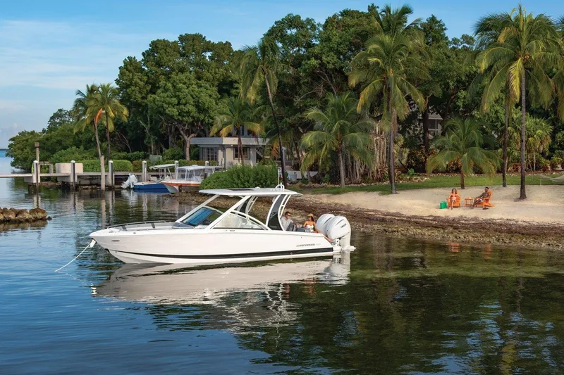 Slide: The Image of 2026 Chaparral 310 OSX boat near tropical beach with palm trees and people relaxing. - 2