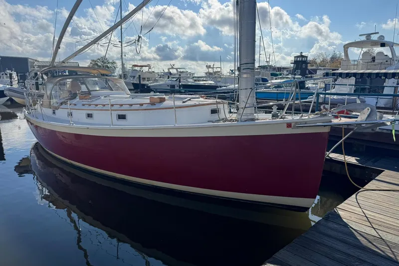 Slide: The Image of 1988 Nonsuch 36 sailboat with red hull docked at marina under blue sky. - 35