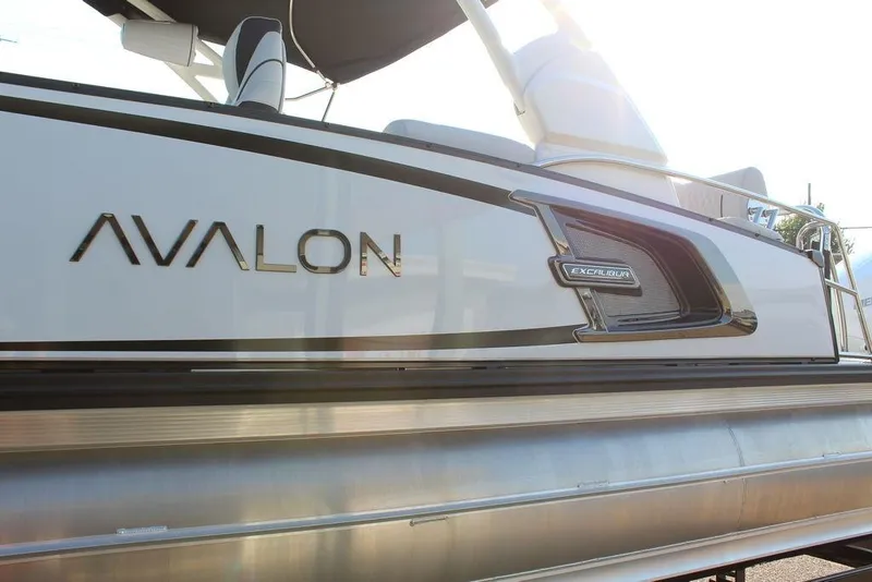 Slide: The Image of 2026 Avalon Excalibur LTD Quad Lounge 25 FT pontoon boat, side view with branding. - 9