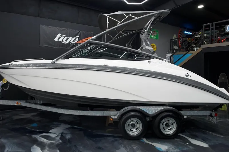 Slide: The Image of 2015 Yamaha Boats 212X on trailer in showroom, sleek design, white and gray exterior. - 2