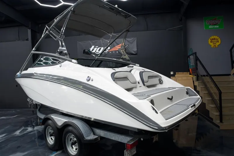 Slide: The Image of 2015 Yamaha Boats 212X on trailer in showroom, sleek design, white and gray color scheme. - 4