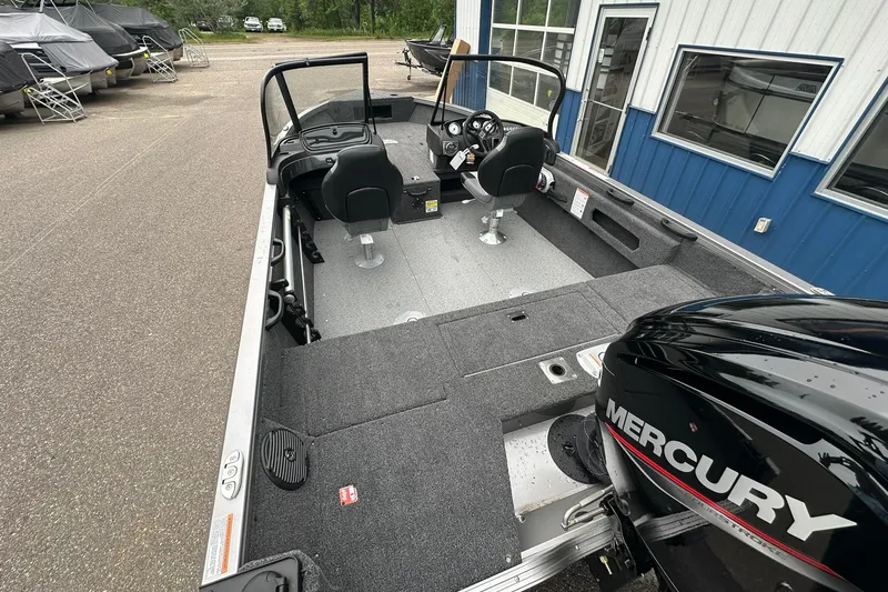 Slide: The Image of 2025 Crestliner 1750 Hawk boat interior with Mercury engine, parked near blue building. - 11