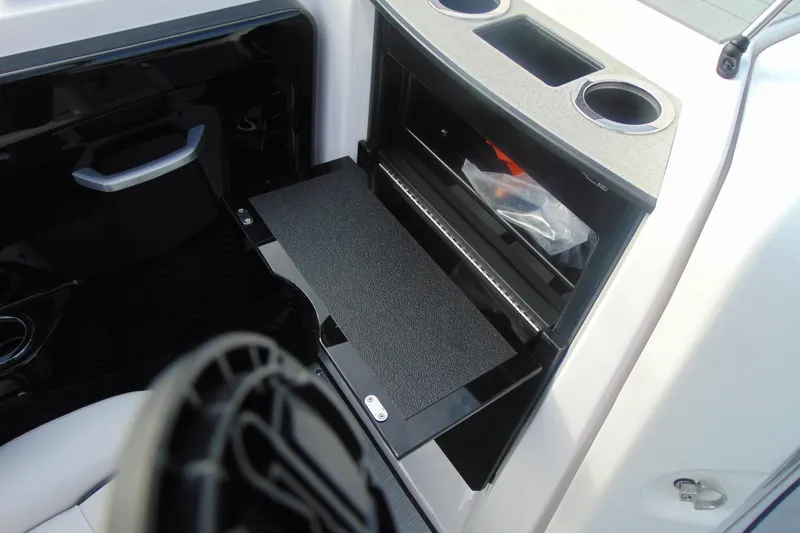 Slide: The Image of 2026 Yamaha Boats AR250 interior storage compartment with cup holders and shelf. - 11
