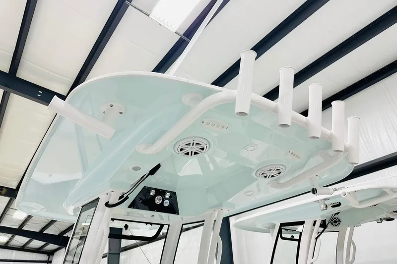 Slide: The Image of 2026 Sportsman Masters 247 Bay Boat T-top with rod holders and speakers in a warehouse. - 7