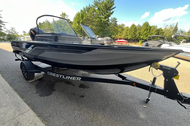 Slide: The Image of 2026 Crestliner 1850 Fish Hawk boat on trailer, parked outdoors, surrounded by trees and other boats. - 4