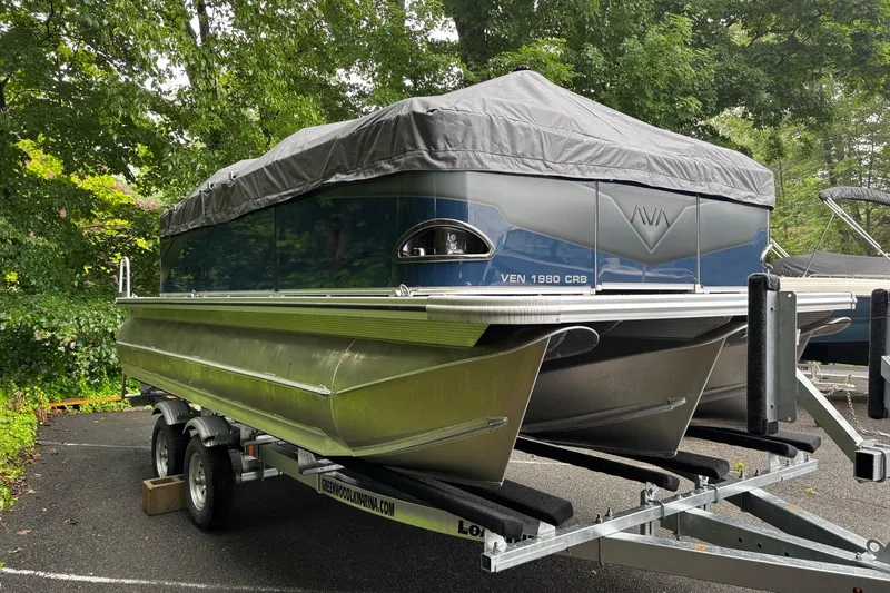 Slide: The Image of 2025 Avalon Venture Cruise Rear Bench pontoon boat on trailer, covered and parked outdoors. - 4