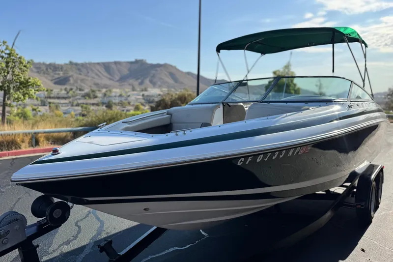 Slide: The Image of 1996 Cobalt 232 boat with green canopy on trailer, scenic mountain background. - 3
