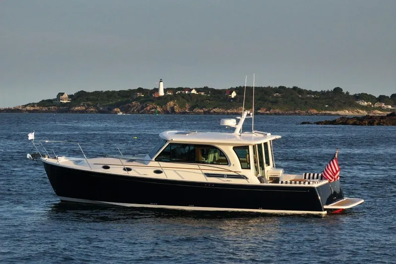 Slide: The Image of Back Cove 412 yacht cruising near a scenic coastline with a lighthouse, 2026 model. - 2