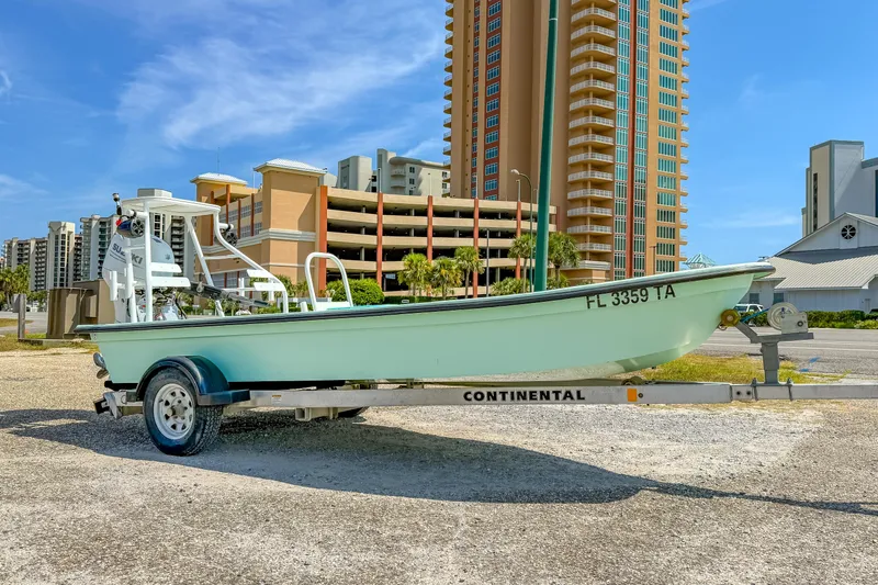 Slide: The Image of 2021 Custom 15' Tiller Skiff on trailer, parked near high-rise buildings under a clear blue sky. - 5
