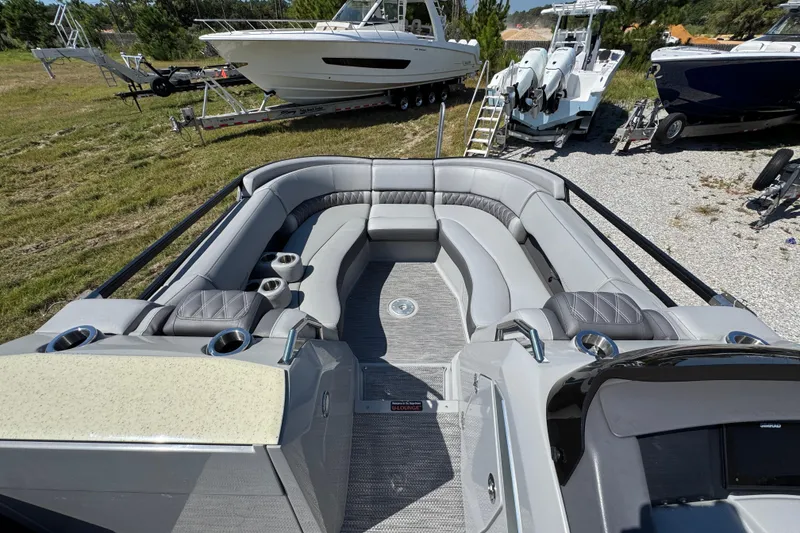 Slide: The Image of 2021 Bennington 25 RTSB boat interior with luxurious seating and cup holders, parked outdoors. - 16