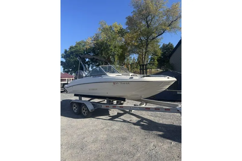 Slide: The Image of 2016 Stingray 191DC (OB) boat on trailer, parked outdoors with trees in background. - 24