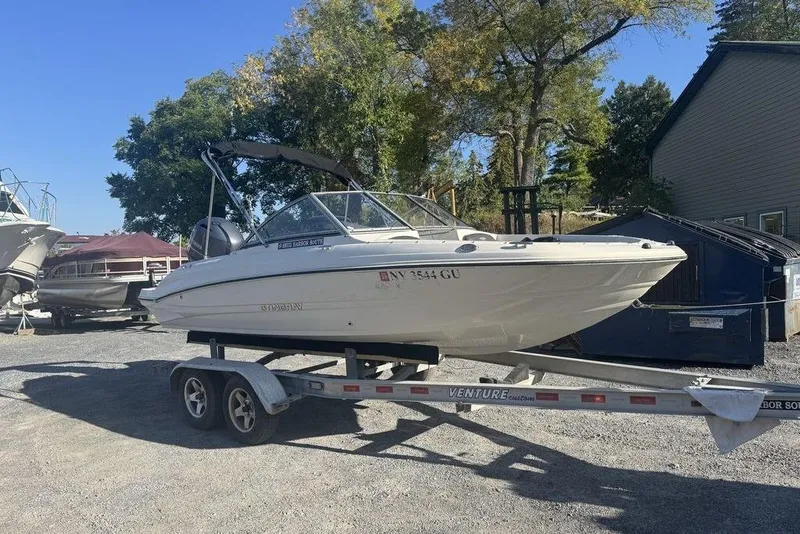 Slide: The Image of 2016 Stingray 191DC (OB) boat on trailer, parked outdoors near trees and buildings. - 25