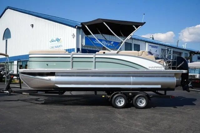 The Image of 2026 Harris Cruiser 210 pontoon boat on trailer, parked outside a marine dealership. - 1