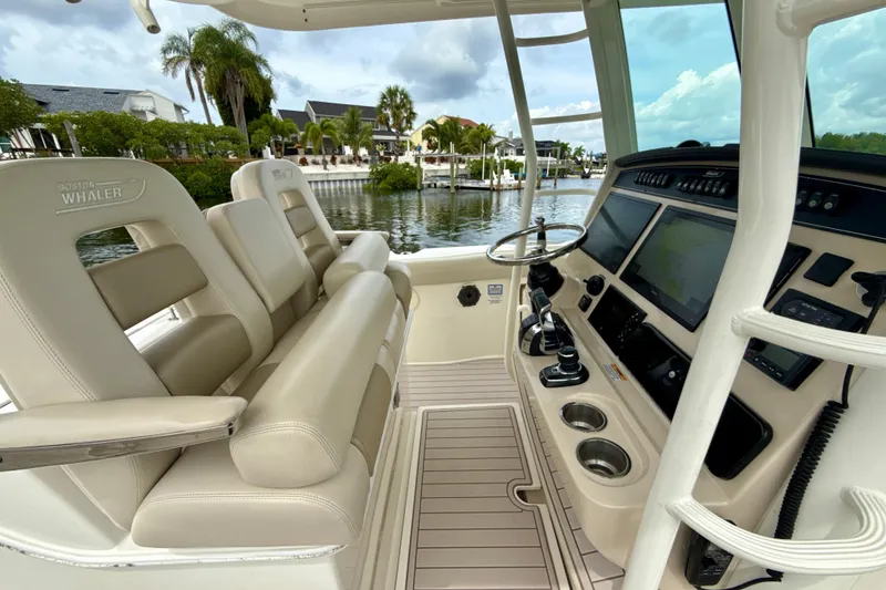 Slide: The Image of 2019 Boston Whaler 330 Outrage boat interior with helm and seating, docked by waterfront homes. - 2