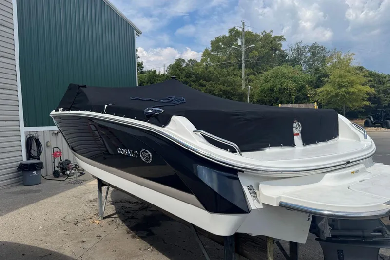 Slide: The Image of 2013 Cobalt 220 boat with black cover, parked outdoors near green building. - 41
