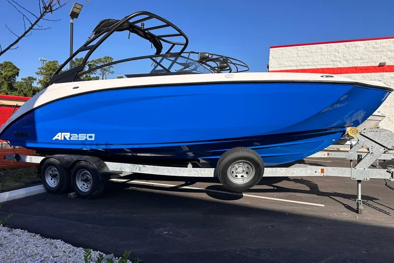 Slide: The Image of 2025 Yamaha Boats AR250 in vibrant blue on a trailer, parked outdoors. - 1