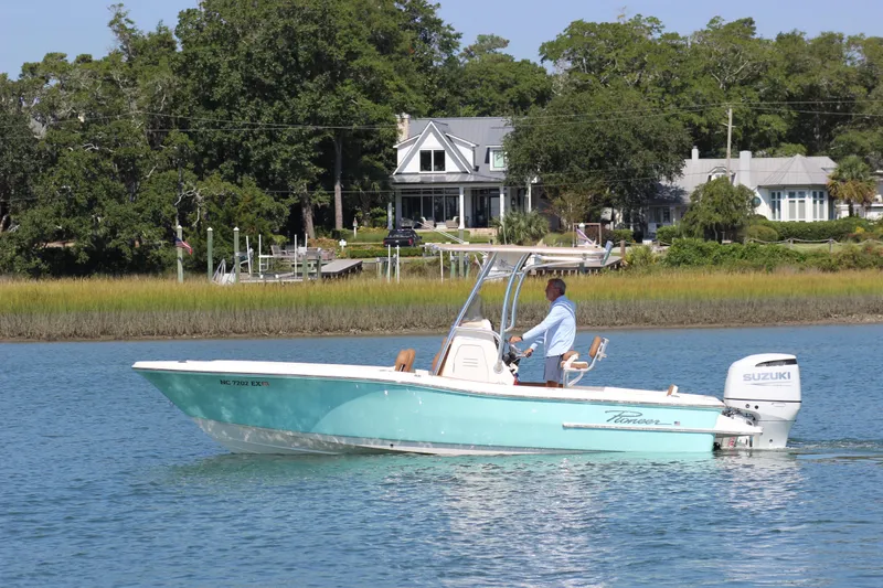 The Image of 2022 Pioneer 220 Bay Sport boat cruising on a serene waterway near a picturesque house. - 1