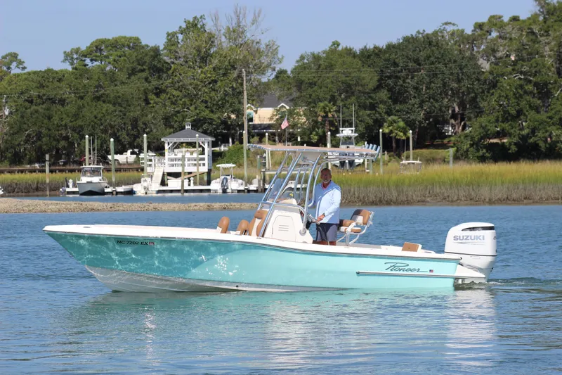 Slide: The Image of 2022 Pioneer 220 Bay Sport boat cruising on a calm river near a marina. - 3