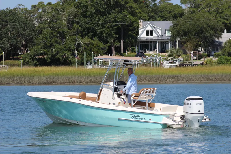 Slide: The Image of 2022 Pioneer 220 Bay Sport boat cruising on a calm river near waterfront homes. - 4