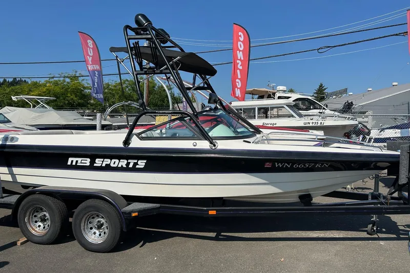 The Image of 1998 MB Boss 210 boat on trailer, displayed outdoors with signage in background. - 0
