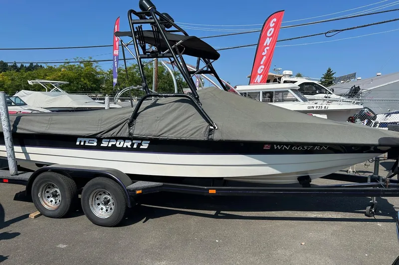 Slide: The Image of 1998 MB Boss 210 boat on trailer, covered, with "MB Sports" branding, parked outdoors. - 2