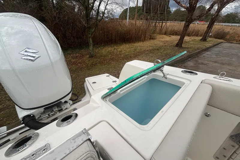 Slide: The Image of 2026 Sailfish 252 CC boat with Suzuki engine and open livewell, parked near trees. - 13