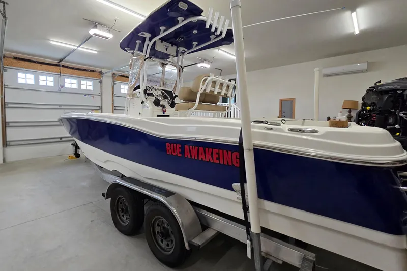 Slide: The Image of 2019 NauticStar 231 Hybrid boat in garage, blue hull, "RUE AWAKENING" text. - 13