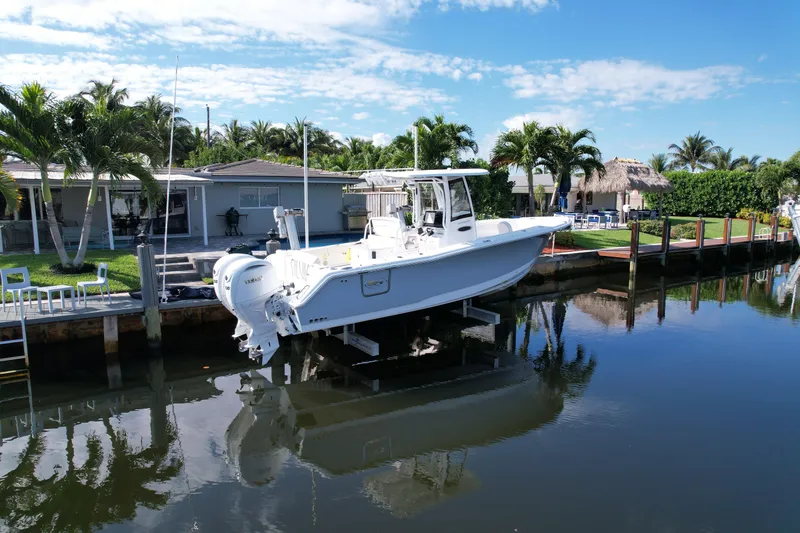 Slide: The Image of 2024 Sea Hunt Ultra 275 SE boat docked by waterfront home, surrounded by palm trees. - 2