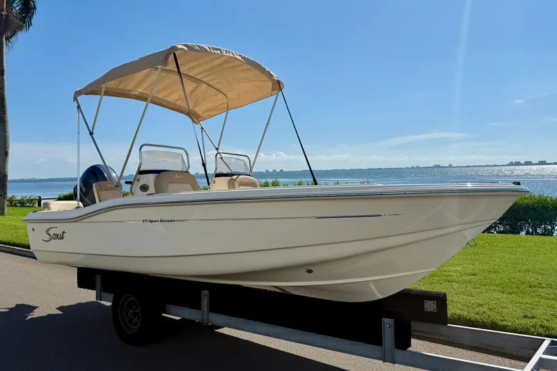 Slide: The Image of 2026 Scout 175 Sport Dorado boat on trailer by waterfront, under clear blue sky. - 2